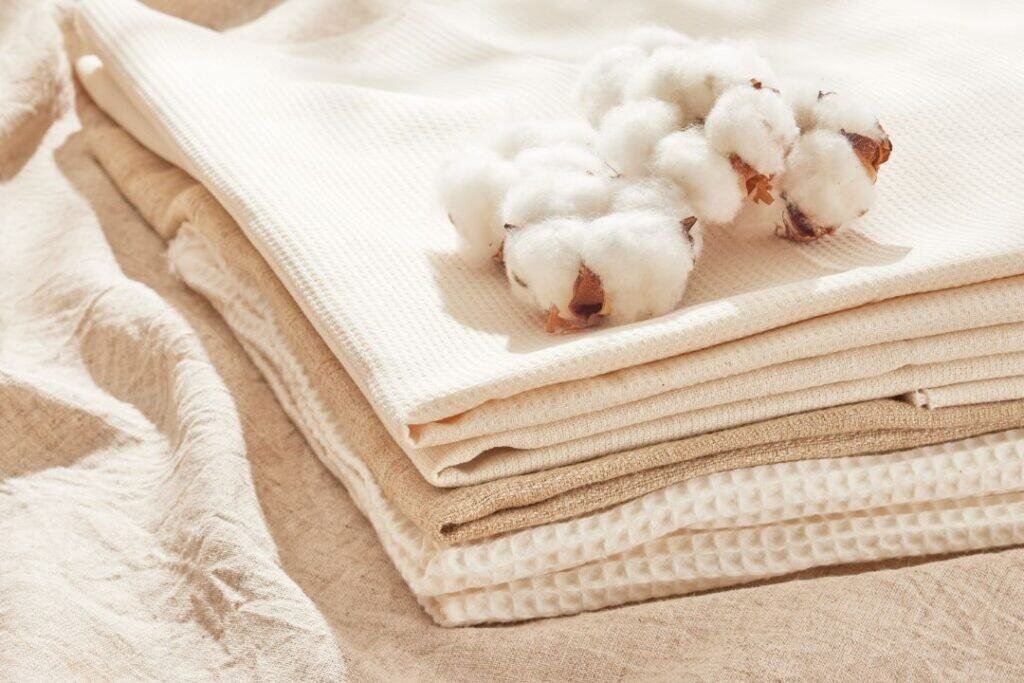 Soft, eco-friendly linens with cotton flowers on neutral-toned fabrics for sustainable, mindful travel and relaxation.