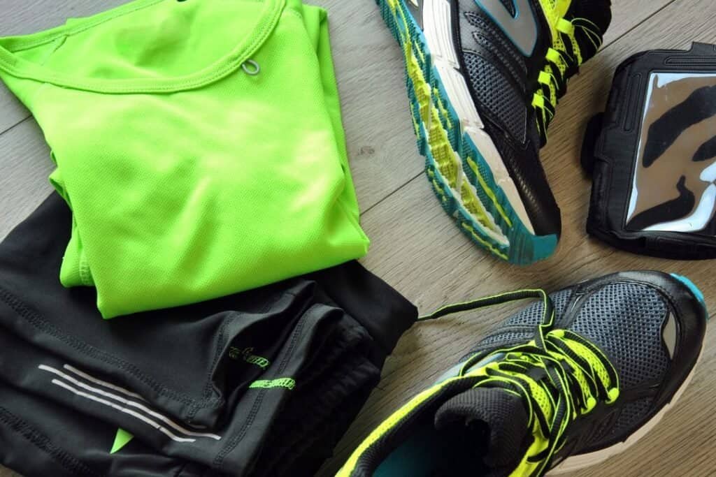Bright neon green athletic shirt and black workout pants with vibrant running shoes, fitness tracker, and portable device, ready for outdoor exercise.