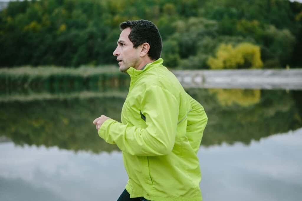 Quiet man jogging by a tranquil lake surrounded by lush greenery, embracing mindful outdoor activities and sustainable adventure.