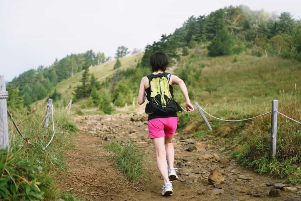 Young woman hiking on a scenic trail in the mountains, wearing a backpack and athletic clothing, embracing mindful outdoor adventure.