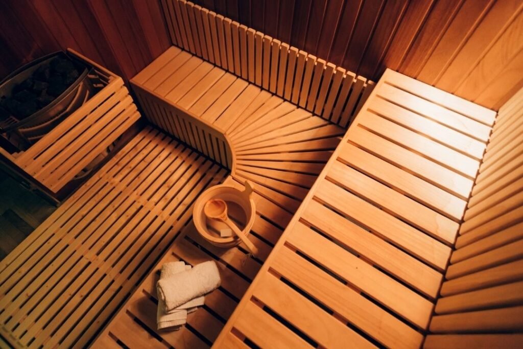 A cozy wooden sauna with curved seating, a bucket with a ladle, and folded towels, promoting sustainable wellness and mindful relaxation.