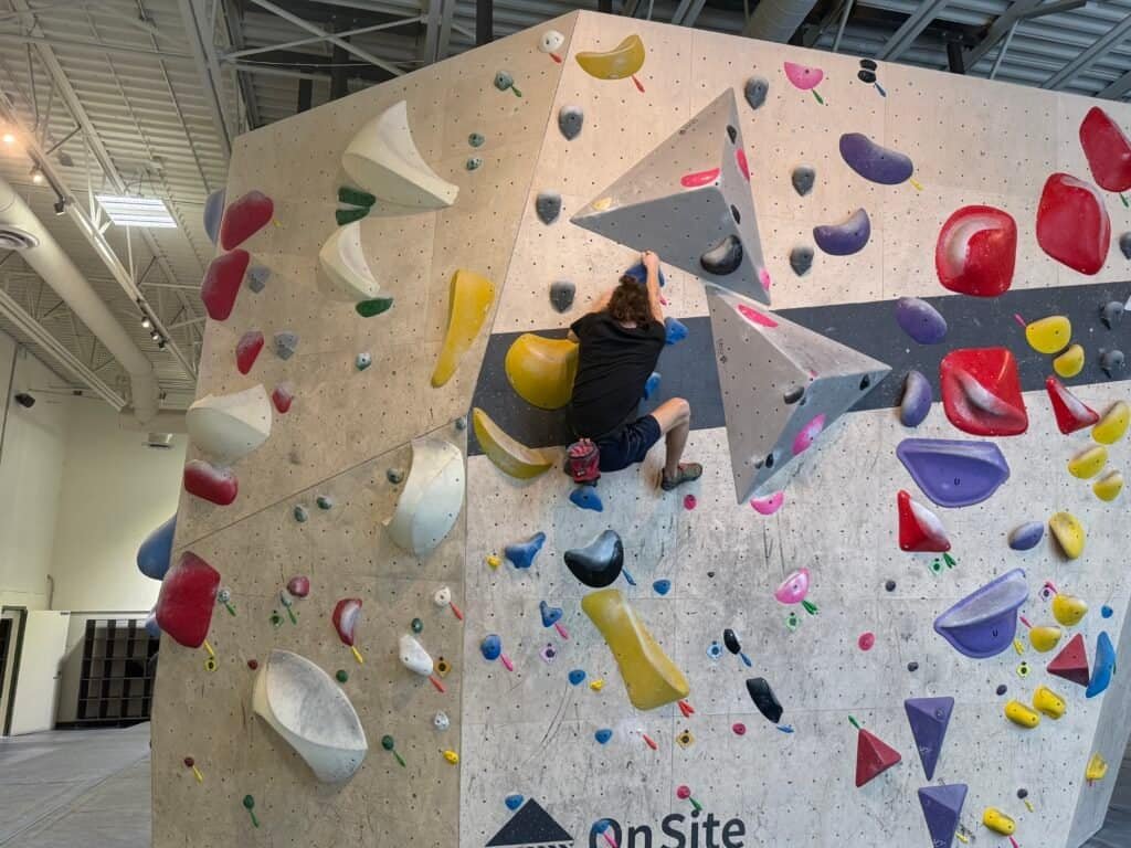 Climber on indoor bouldering wall with climbing gear.