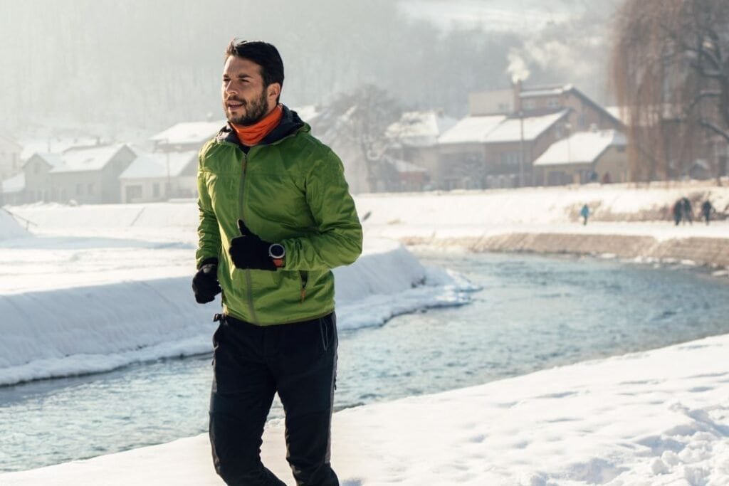 Fresh-faced man jogging in snowy winter landscape with cozy cabins in the background, embracing outdoor adventure and mindful travel amidst nature.