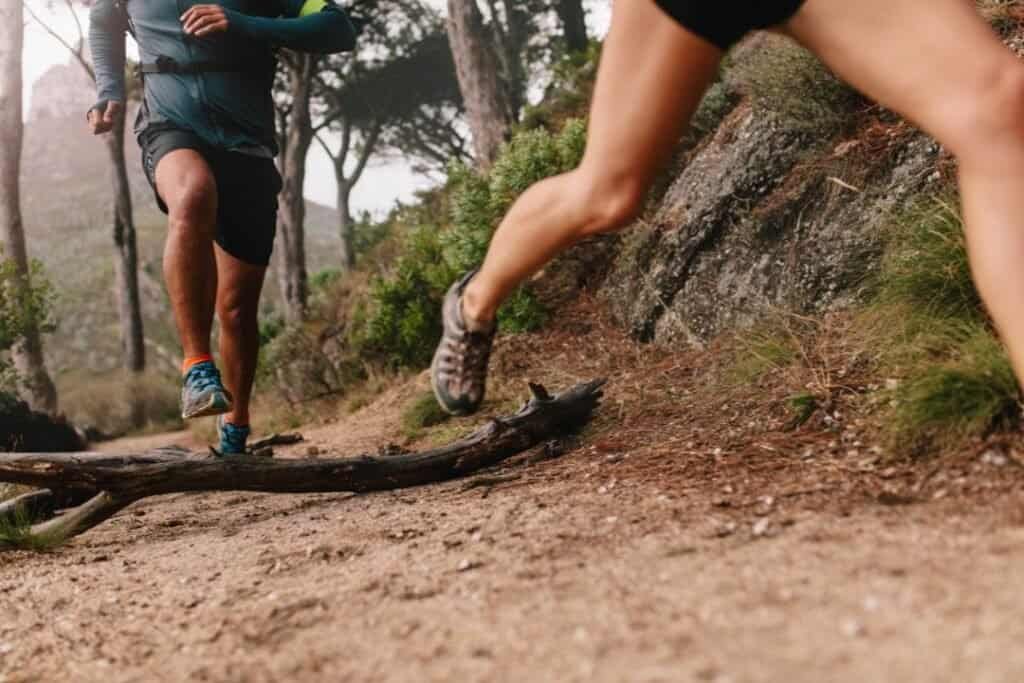 Running on a forest trail with lush greenery and rocky terrain, showcasing active outdoor exploration and mindful adventure.