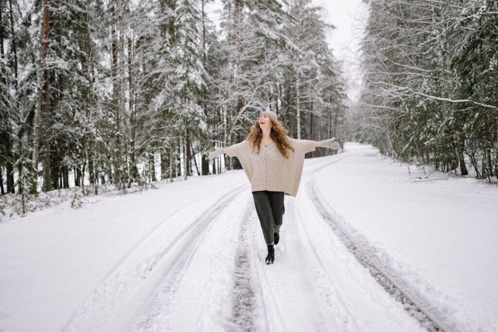 A woman walking barefoot on snow-covered forest trail, connecting with nature and practicing mindful, sustainable travel.