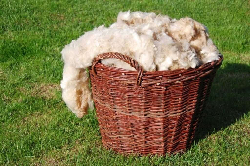Soft wool in a wicker basket on green grass, showcasing sustainable natural materials and eco-friendly handcrafted textiles.