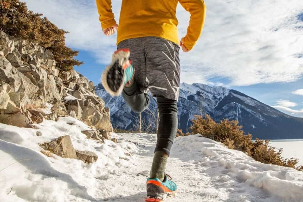 A person running on a snowy mountain trail, wearing thermal leggings and outdoor gear, surrounded by scenic winter landscape.
