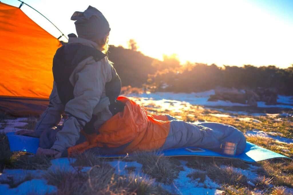 A person resting outdoors at sunset near a tent, connecting with nature and practicing mindful, sustainable travel in a seren.
