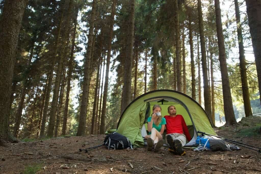 A green camping tent set up in a lush forest, with two hikers sitting outside, enjoying the peaceful natural environment, pro.