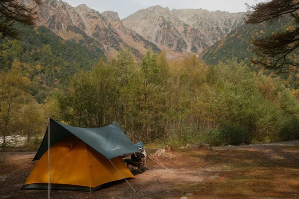 A cozy camping tent set up in a serene, natural environment surrounded by trees and mountains, promoting grounding and connec.