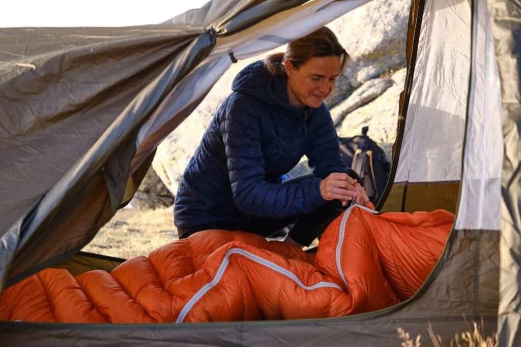 Woman setting up a sleeping bag in a tent during a mindful, eco-friendly backpacking trip in nature.