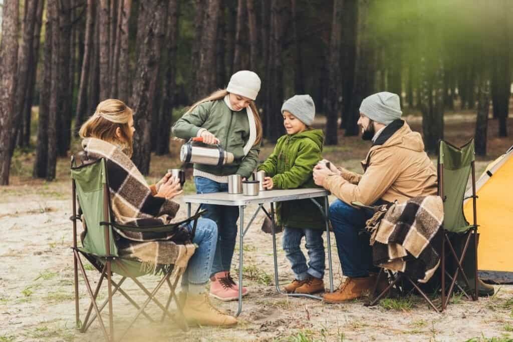 A family enjoying a sustainable camping experience with a portable table in a forest setting, emphasizing connection with nat.