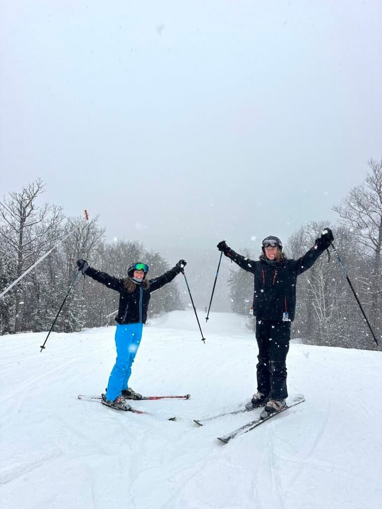 Two skiers with their arms raised on a snowy slope